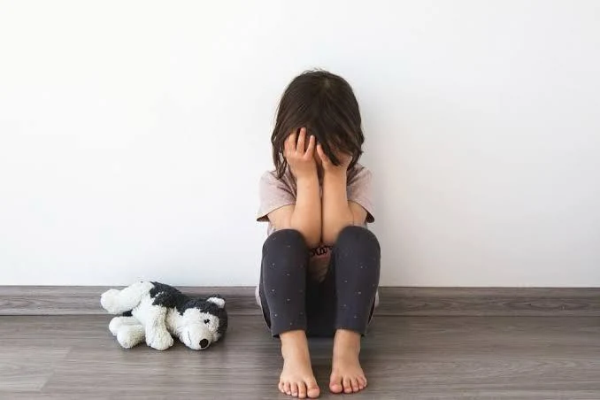 A distressed child sitting beside a stuffed toy